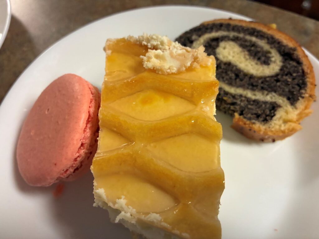 Kat's Wigilia Desserts having a passion fruit macaroon, slice of peach cheesecake, and honey poppyseed strudel served on a white plate.