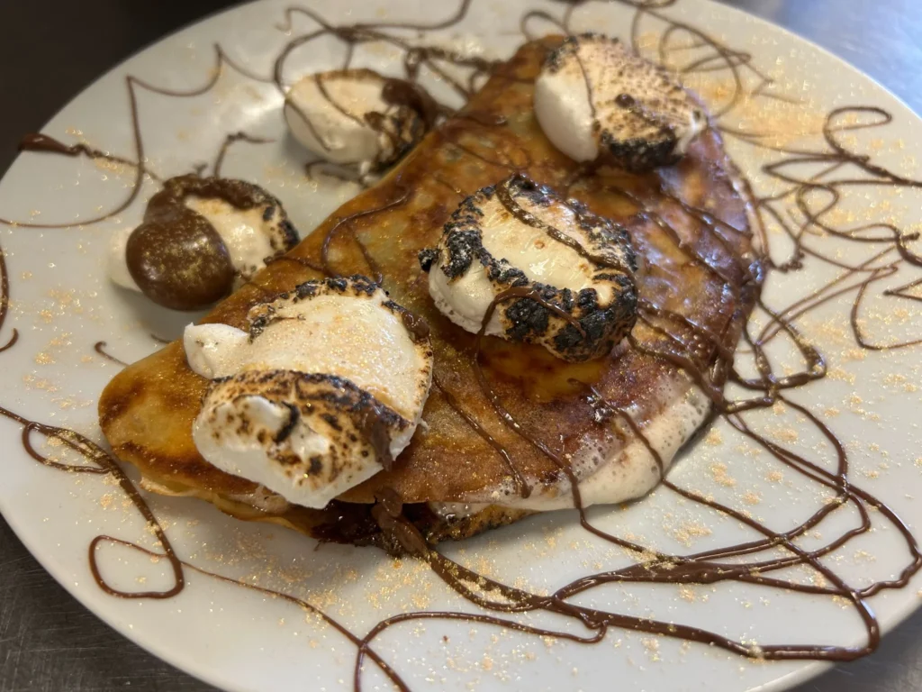 Folded dessert crepe topped with toasted marshmallows and drizzled with chocolate and caramel on a white plate at Kat’s Café & Restaurant.