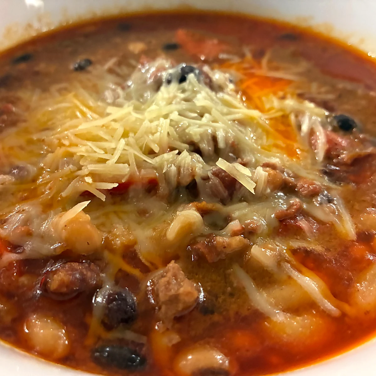 Hearty beef and bean chili topped with shredded cheese in a white bowl.