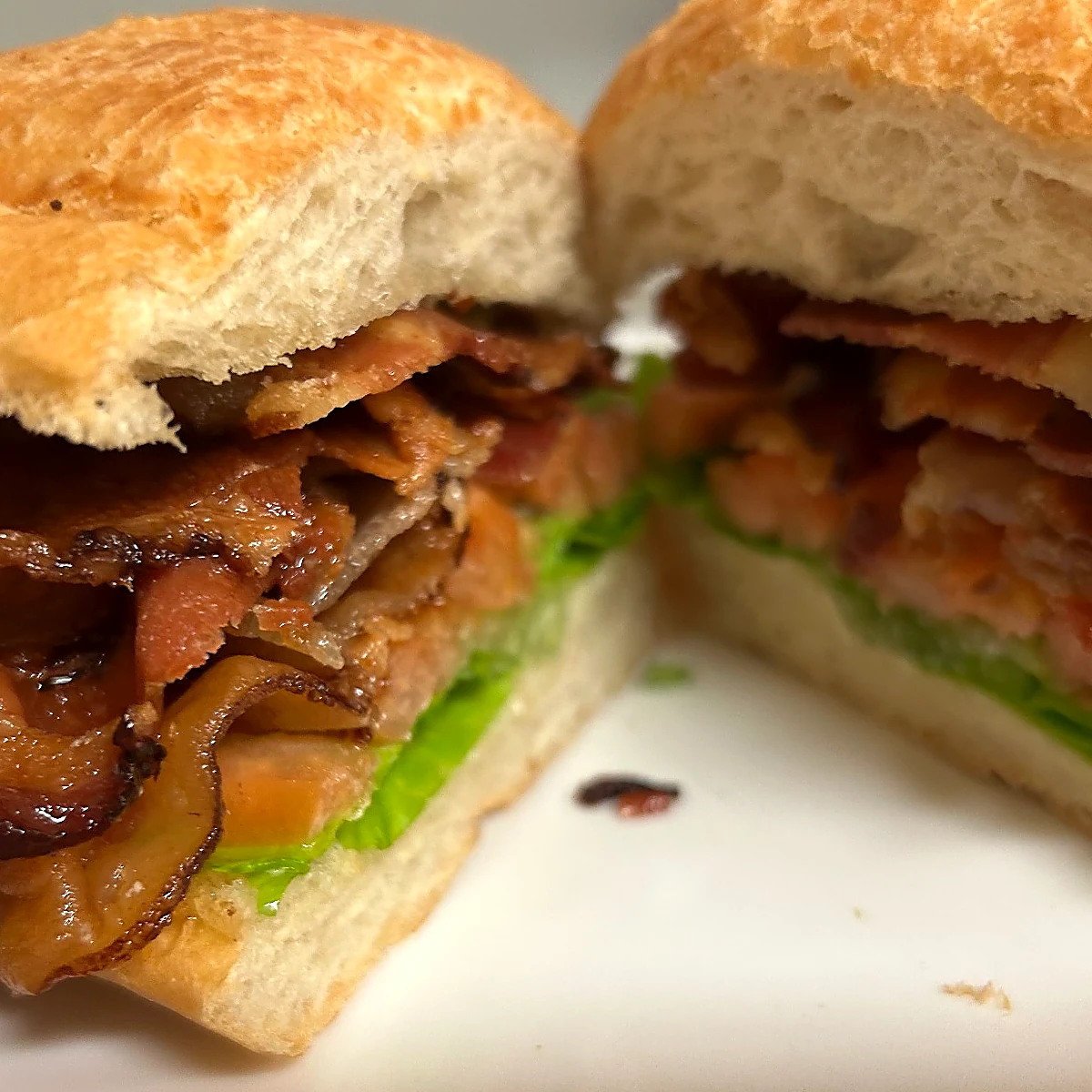 BLT sub cut in half on a white plate, piled with crispy bacon, lettuce, and tomato on a hoagie roll.