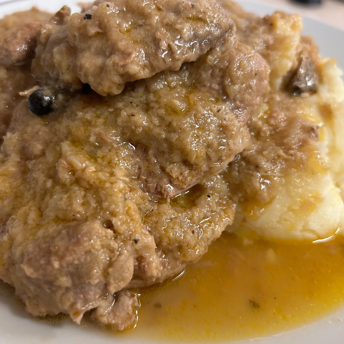 Braised pork in savory natural gravy juices served over mashed potatoes on a plate.