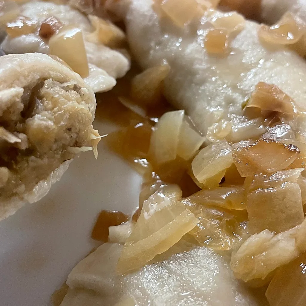 Cabbage and mushroom pierogi with sautéed onions; one pierogi is lifted to show the filling.