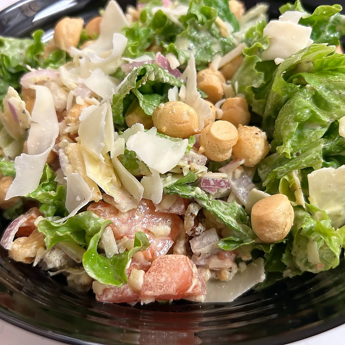Caesar-style salad with shaved parmesan and croutons in a black bowl.