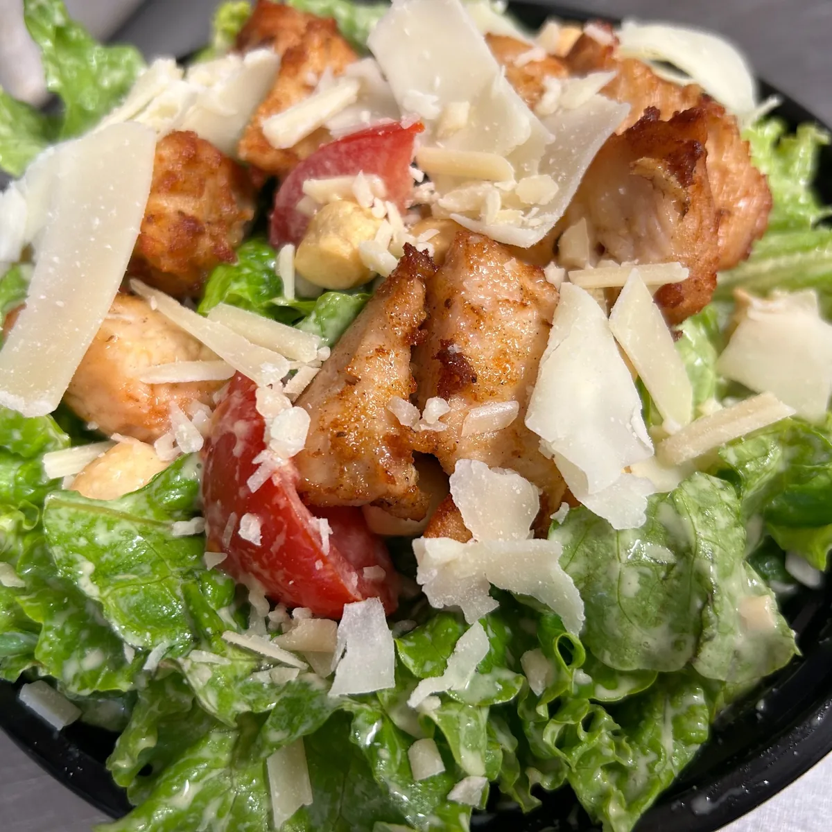 Chicken Caesar salad with grilled chicken and shaved parmesan in a black bowl.