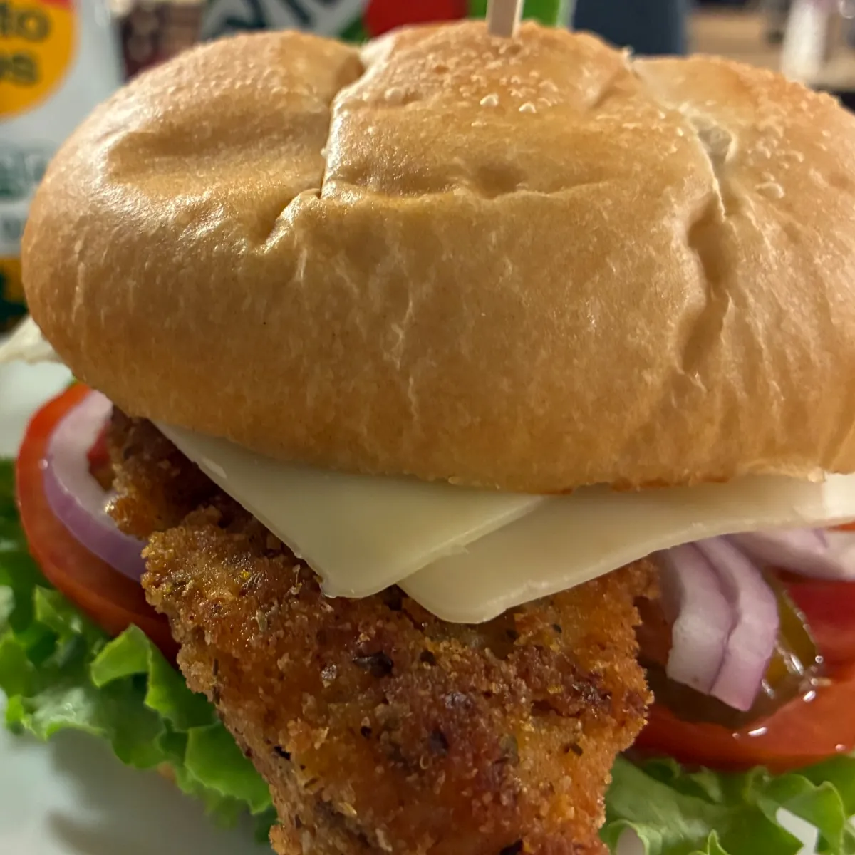 Breaded chicken cutlet sandwich with cheese, lettuce, tomato, and red onion on a roll.