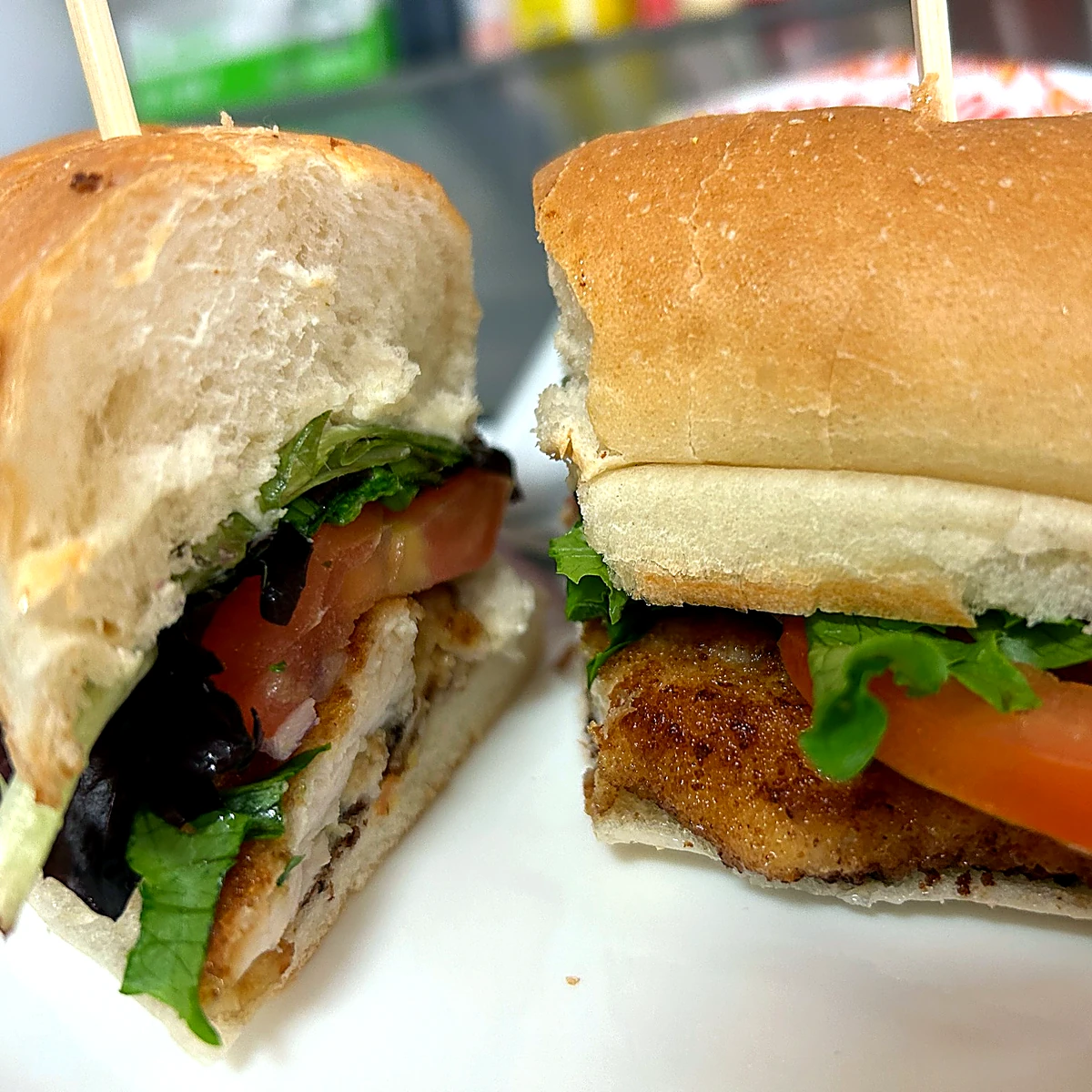 Chicken cutlet sub cut in half with lettuce, tomato, and red onion on a white plate.