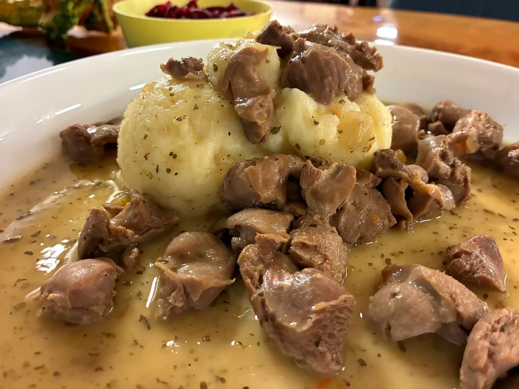 Chicken gizzards in natural gravy served with mashed potatoes on a plate and side bowl of shredded beets.