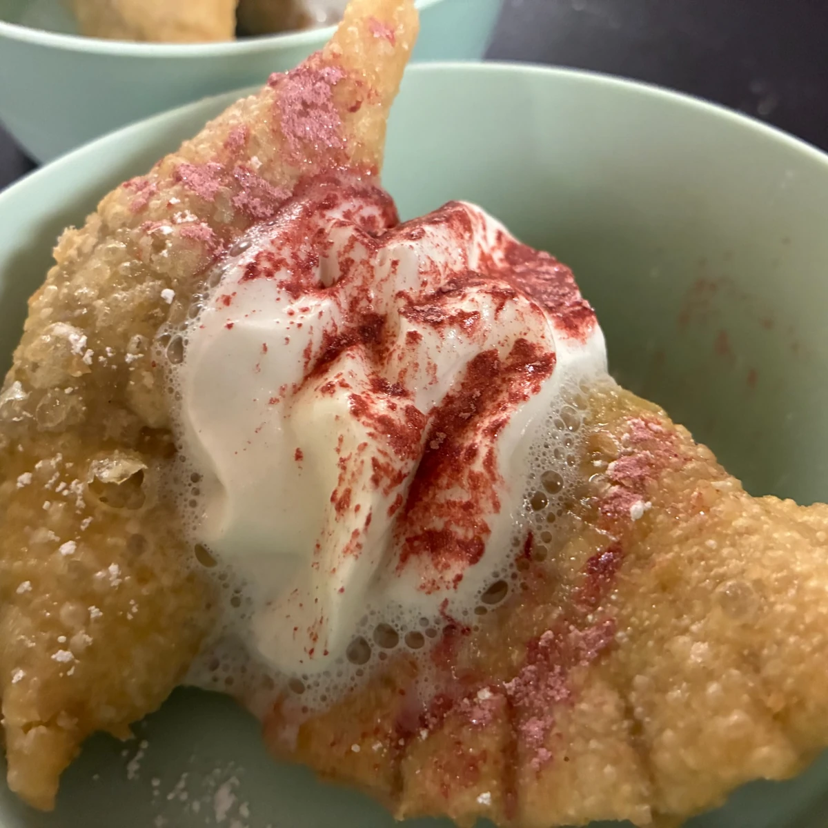 A golden Christmas holiday event pierogi in a bowl topped with whipped cream and red sugar crystals.