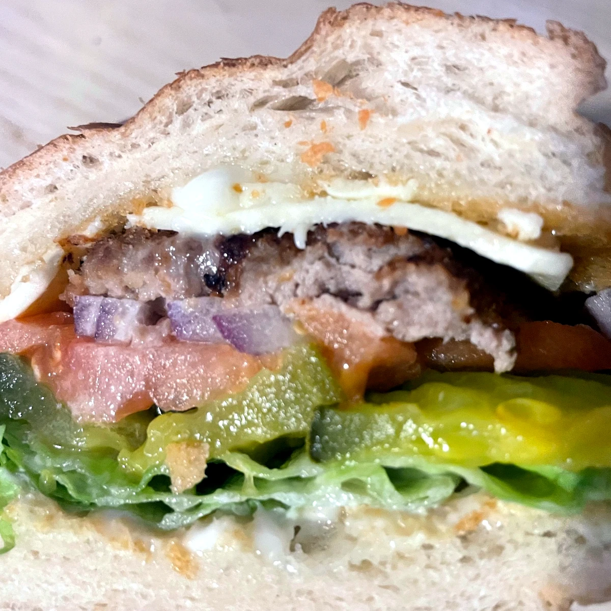 Close-up of a patty schnitzel city chicken sub sandwich with melted cheese, pickles, tomato, red onion, and lettuce on a hoagie roll.