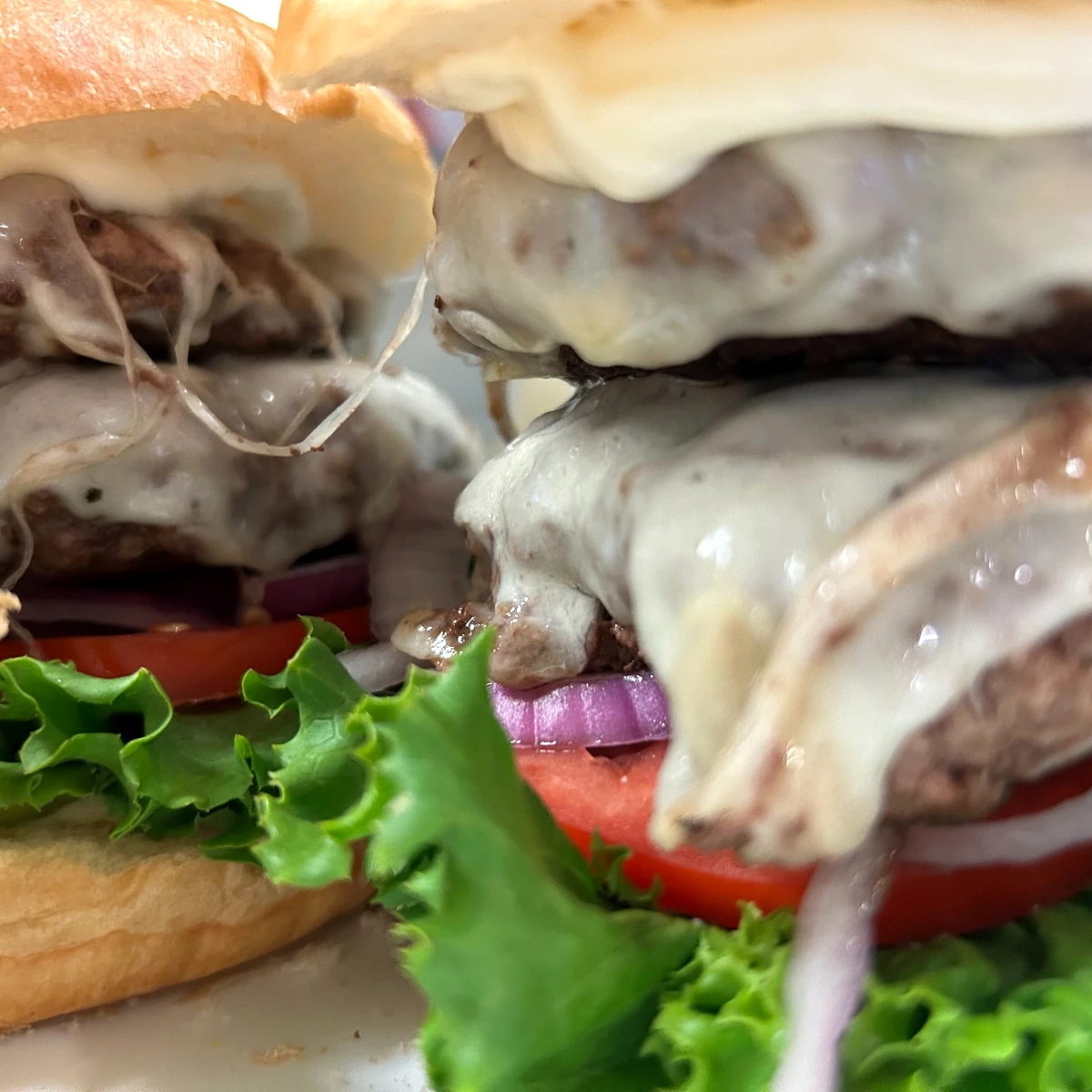 Close-up of a double smash patty burger with melted cheese, lettuce, tomato, and red onion on a bun.