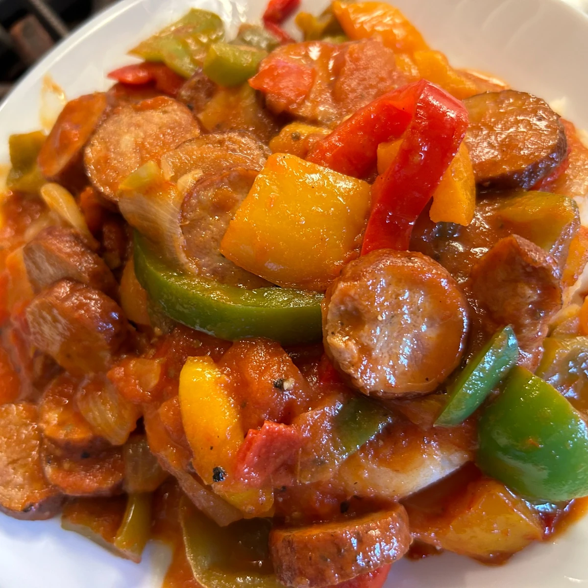 Sliced kielbasa with bell peppers and onions in tomato sauce served over mashed potatoes on a plate.