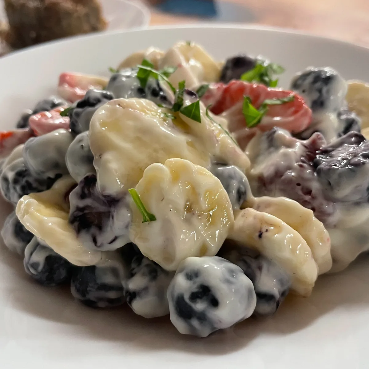 Fruit salad with blueberries, strawberries, blackberries, and banana slices in cream, served in a white bowl.