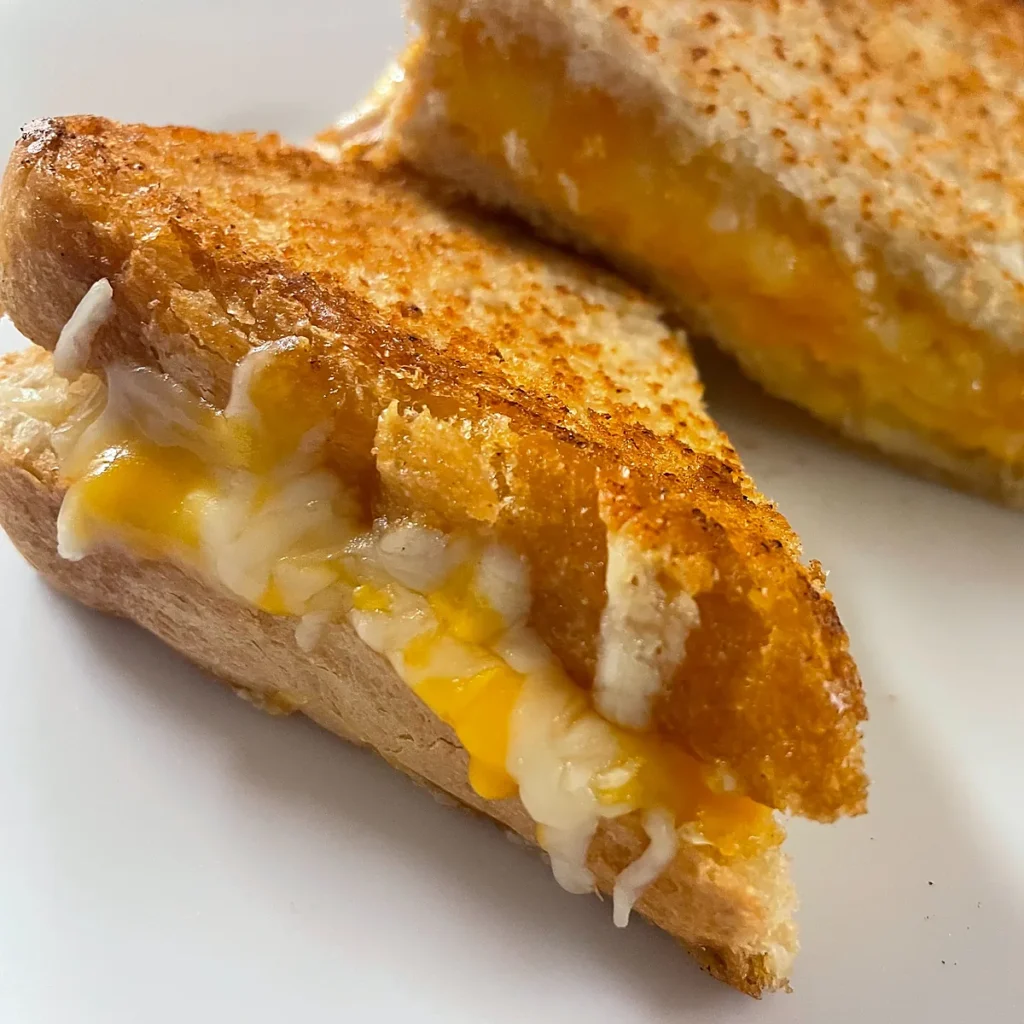 Grilled cheese sandwich halves with melted cheese on a white plate.