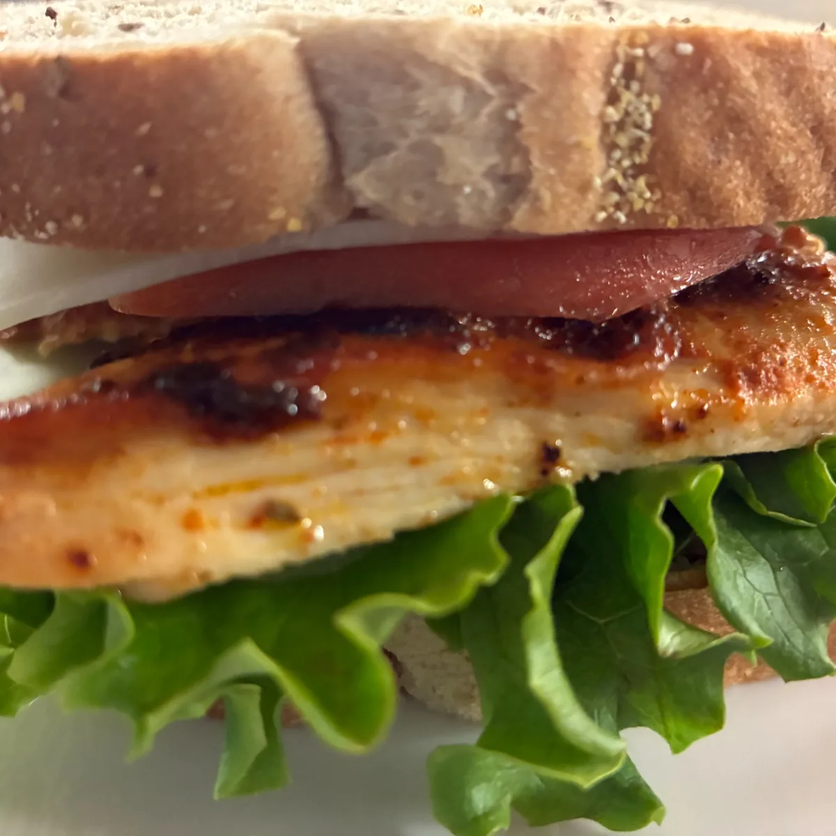 Close-up of a grilled chicken sandwich on rye bread with lettuce, cheese, and tomato.