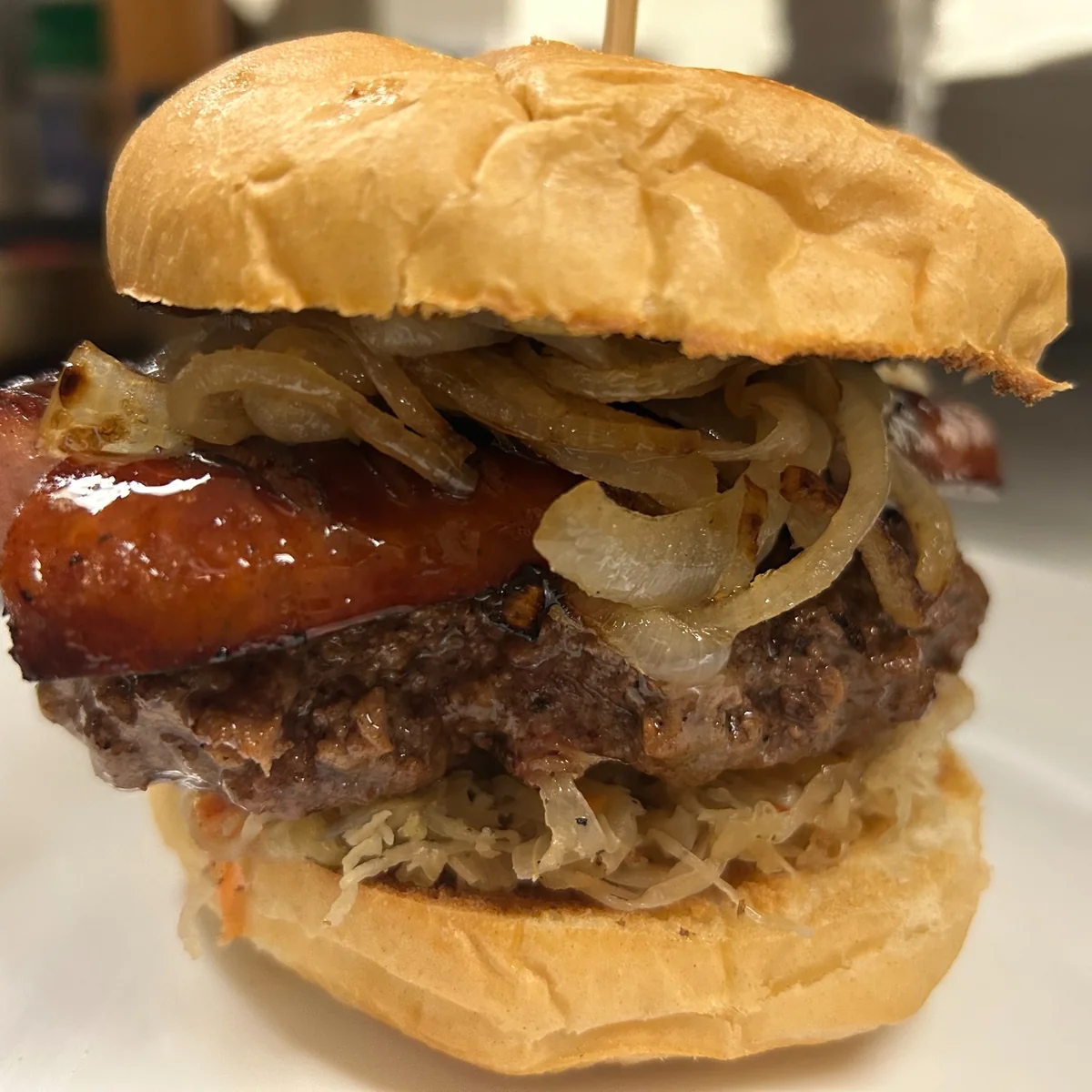 Kielbasa burger on a bun with a real smash burger patty, grilled kielbasa, caramelized onions, and homemade sauerkraut.