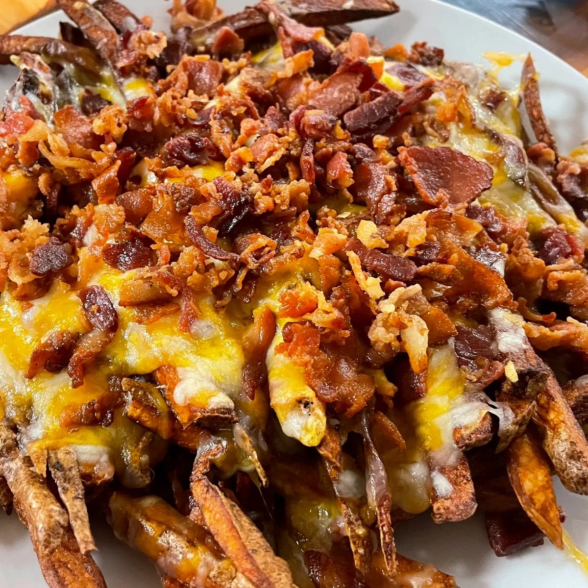 Loaded fries topped with melted cheese and bacon on a white plate.