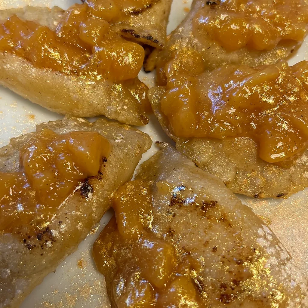 Pan-fried peach pierogi topped with warm homemade peach compote on a white plate.