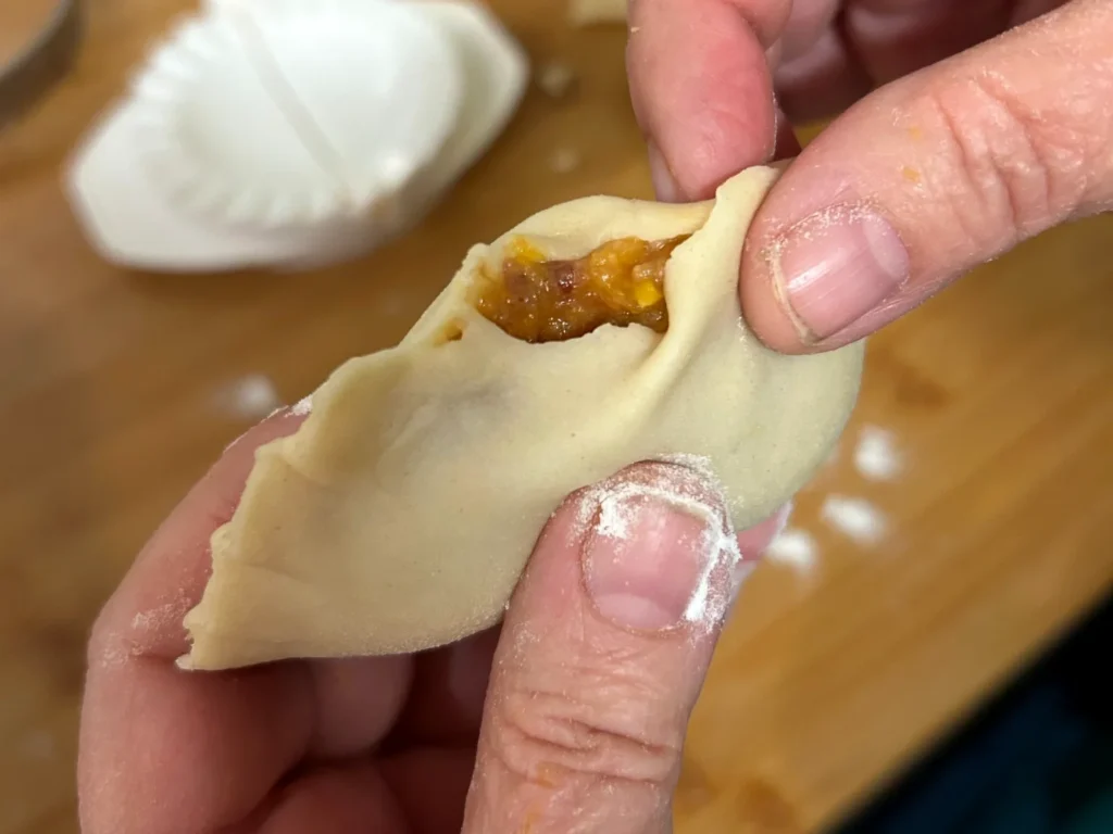 Close-up of hands hand-crimping a pierogi with the filling visible.