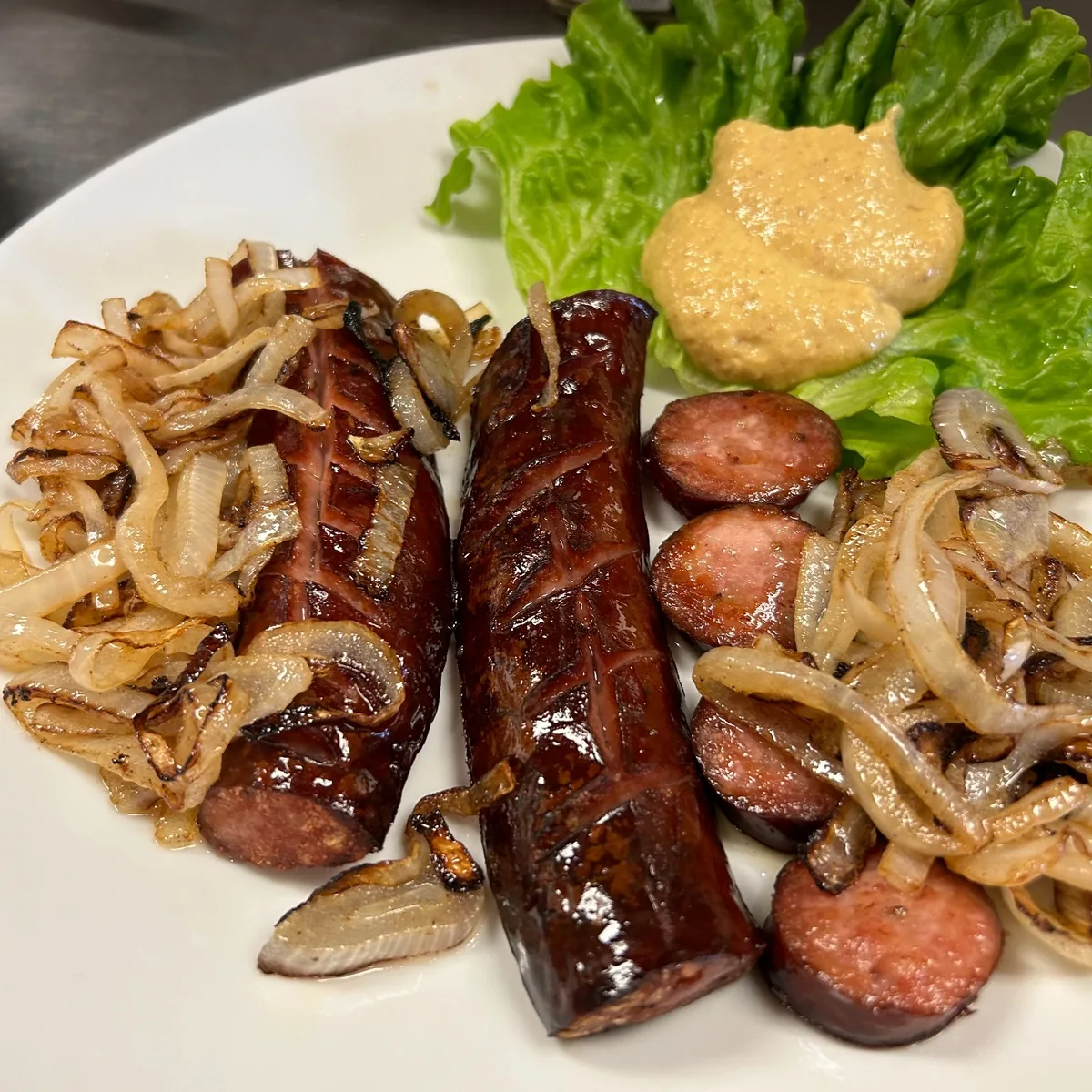 Seared kielbasa with sautéed onions and Slavic mustard served on lettuce on a white plate.