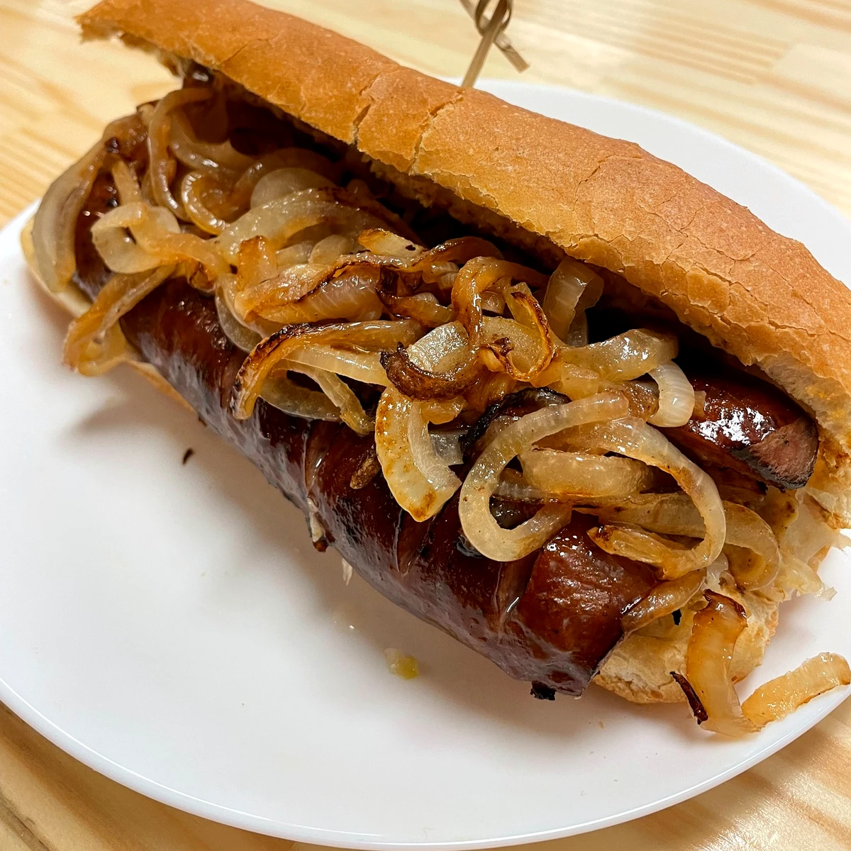 Polish kielbasa sub topped with sautéed onions and Slavic mustard on a hoagie roll, served on a white plate.