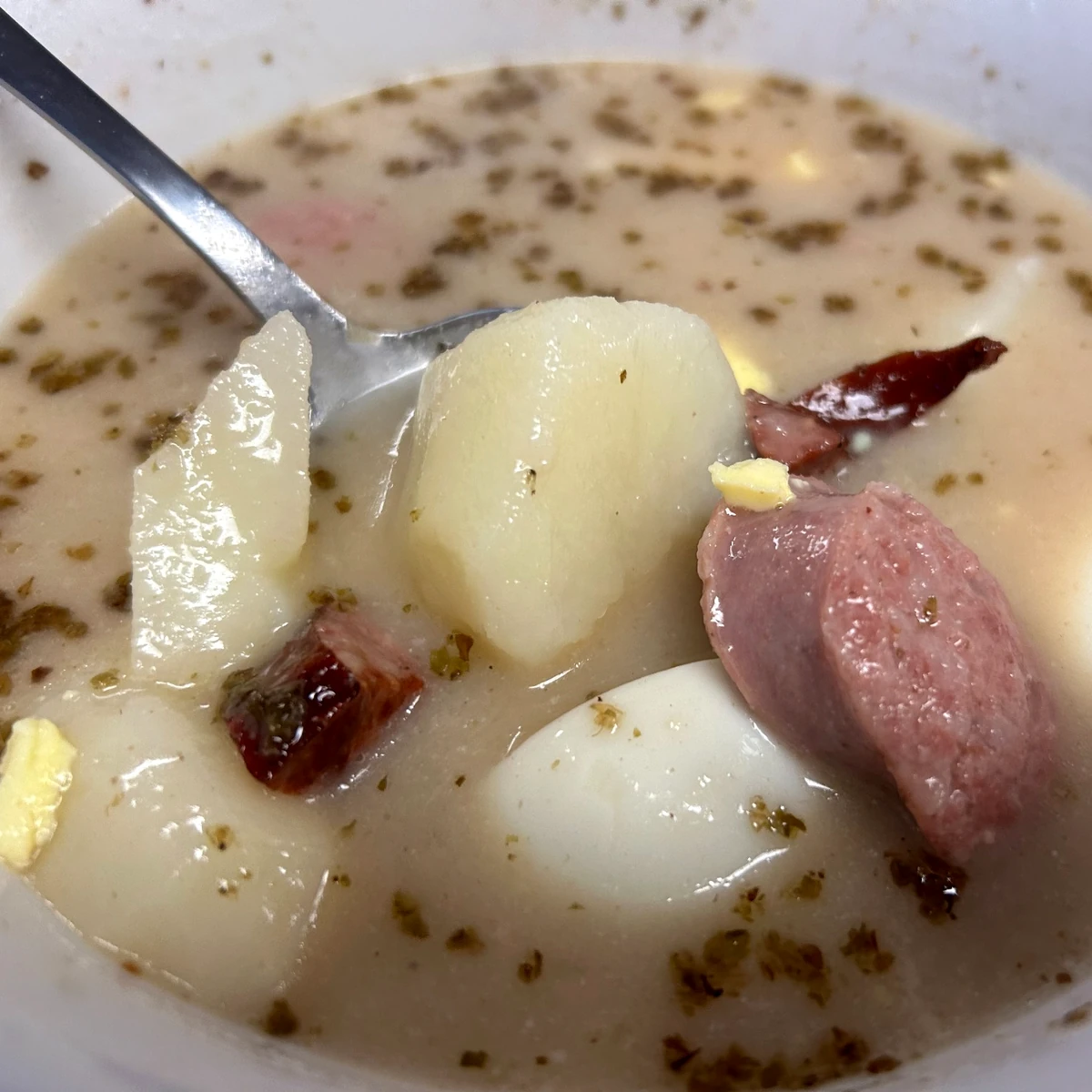 Bowl of Polish żurek soup with sausage, potatoes, and egg in a creamy broth.