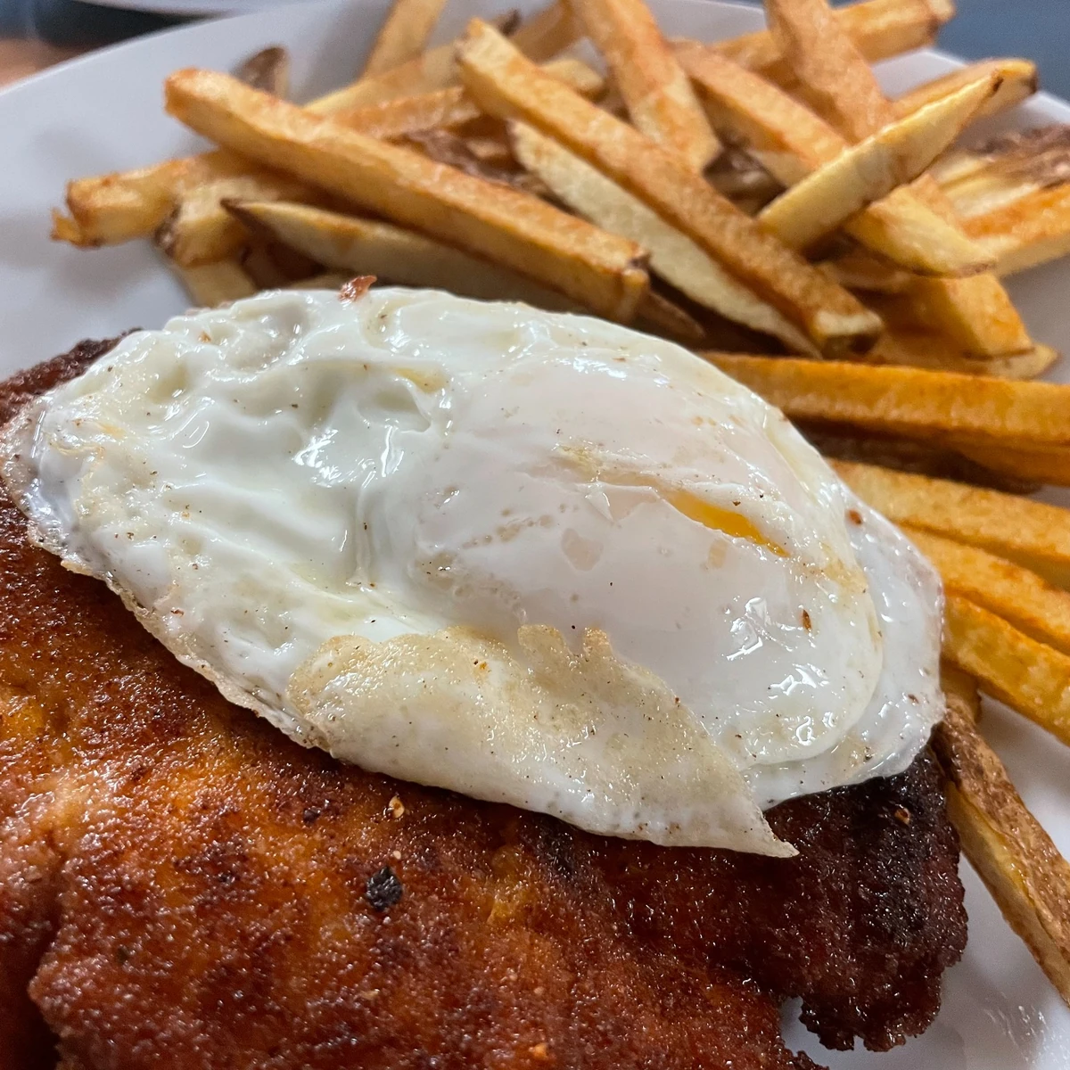 Crispy breaded pork cutlet (pork schnitzel) topped with a fried egg, served with golden fresh-cut fries.