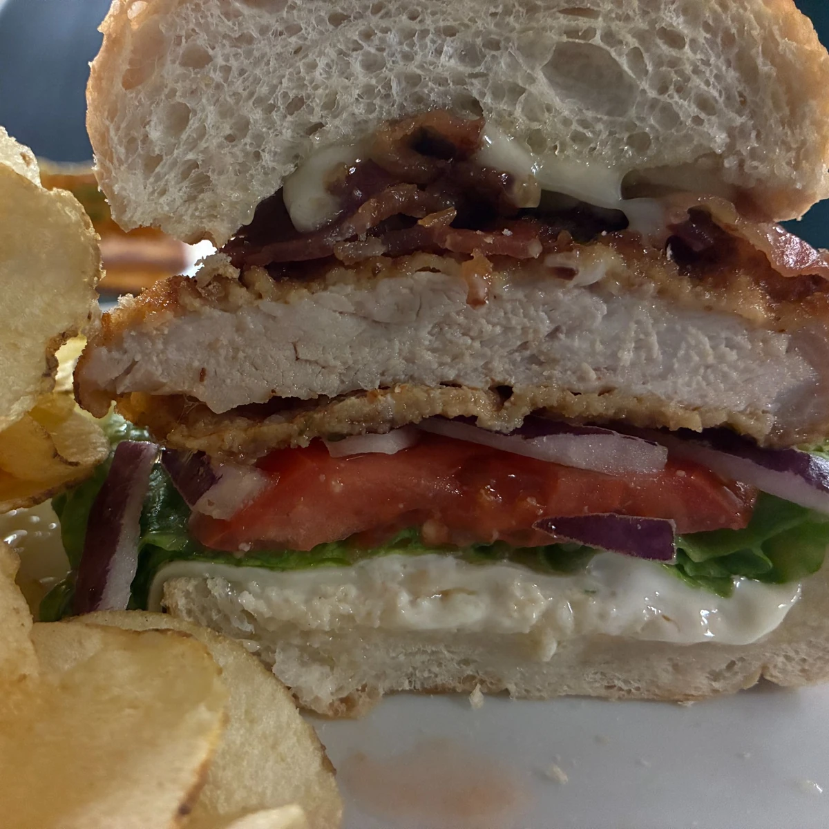 Close-up of a pork schnitzel sub cut in half with lettuce, tomato, red onion, and mayo, with potato chips on the side.