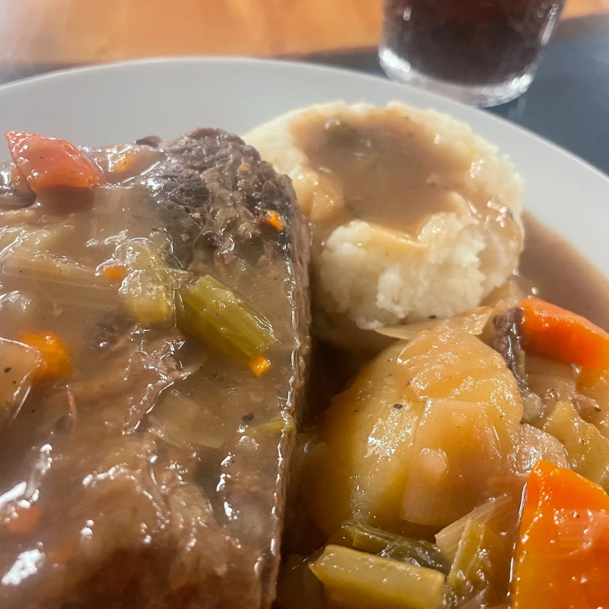 Pot roast covered in savory gravy served with mashed potatoes and vegetables on a plate.