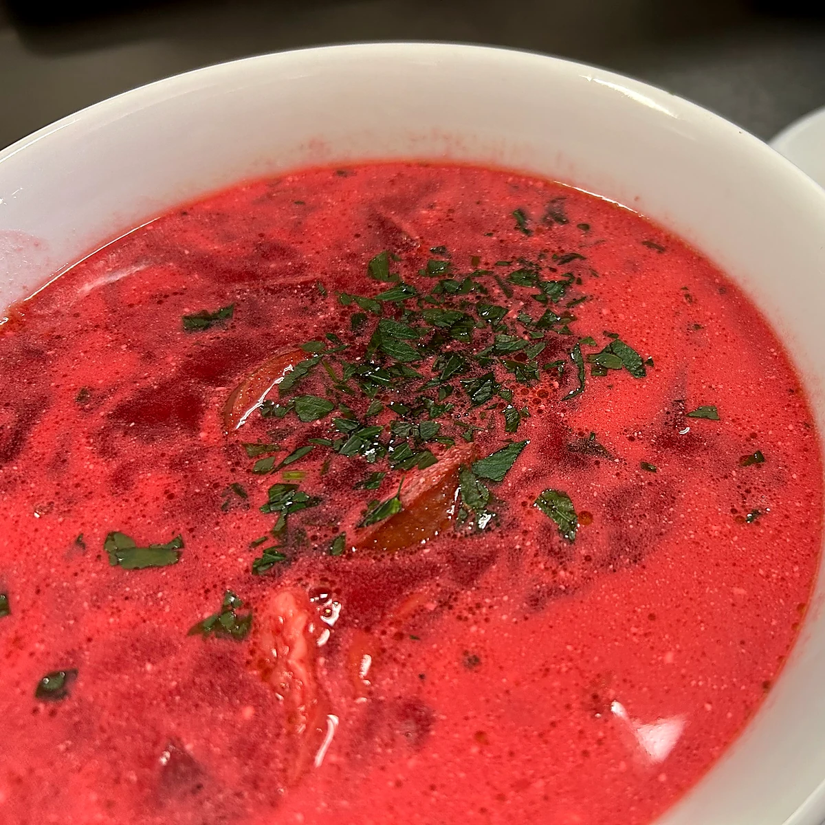 Bowl of bright red beet borscht topped with chopped fresh herbs.