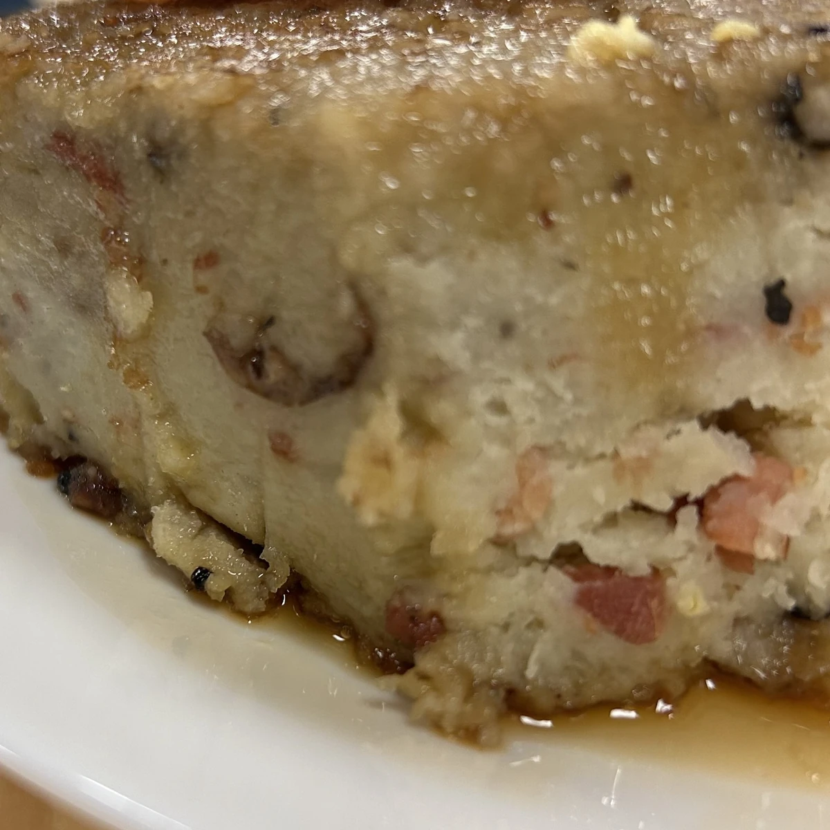 Close-up of a thick slice of savory baked potato, onions, and bacon casserole-like babka on a white plate with maple syrup juices.