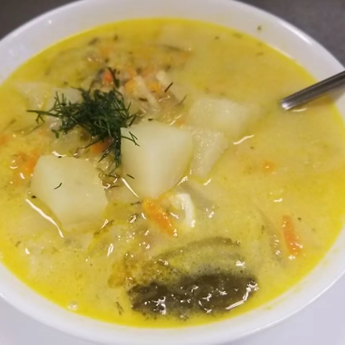 Creamy shredded pickle soup (ogórkowa zupa) with potato chunks and fresh dill in a white bowl, with a spoon.