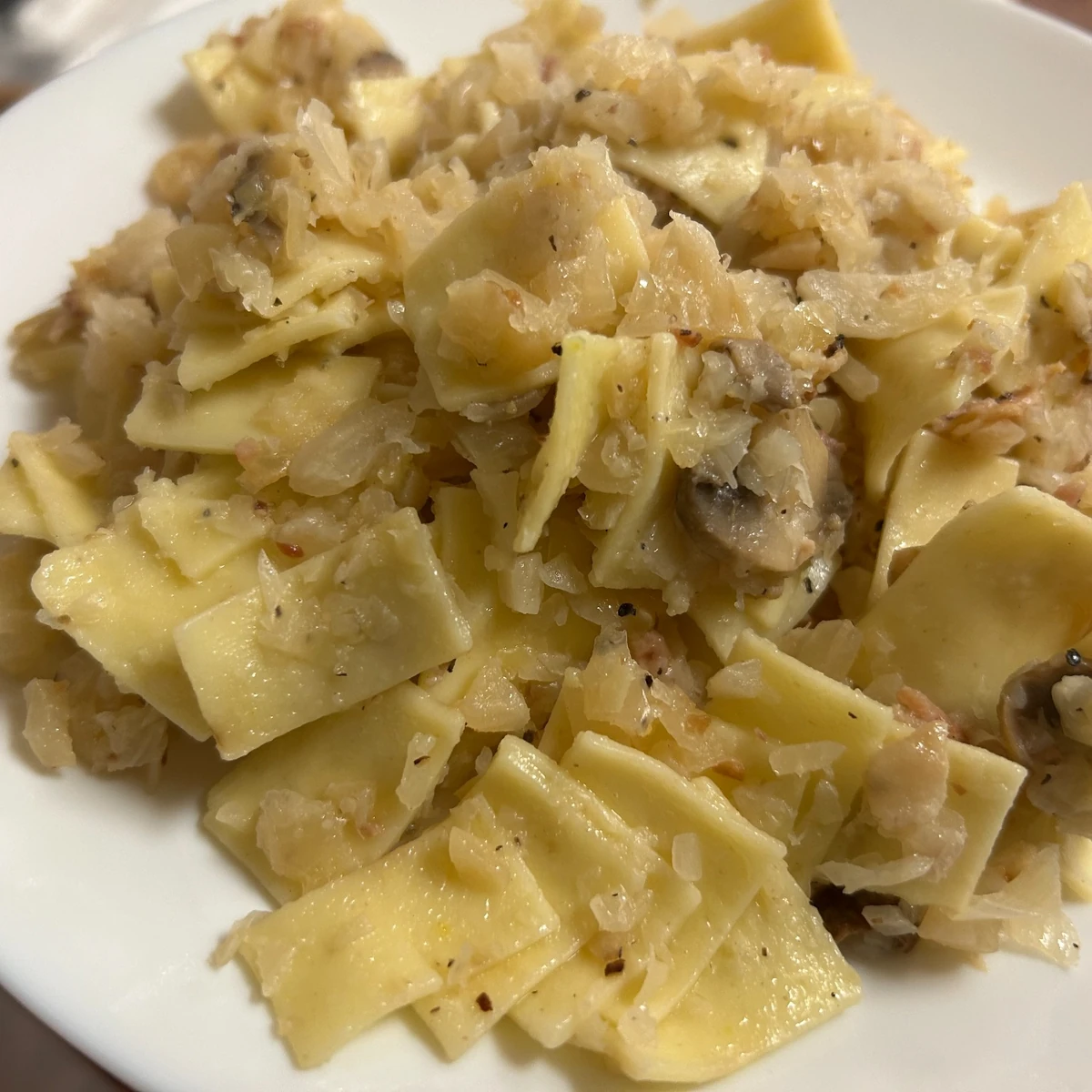 Haluski noodles tossed with sautéed cabbage, mushrooms, onions, and bacon, served on a white plate. Also known as "łazanki."