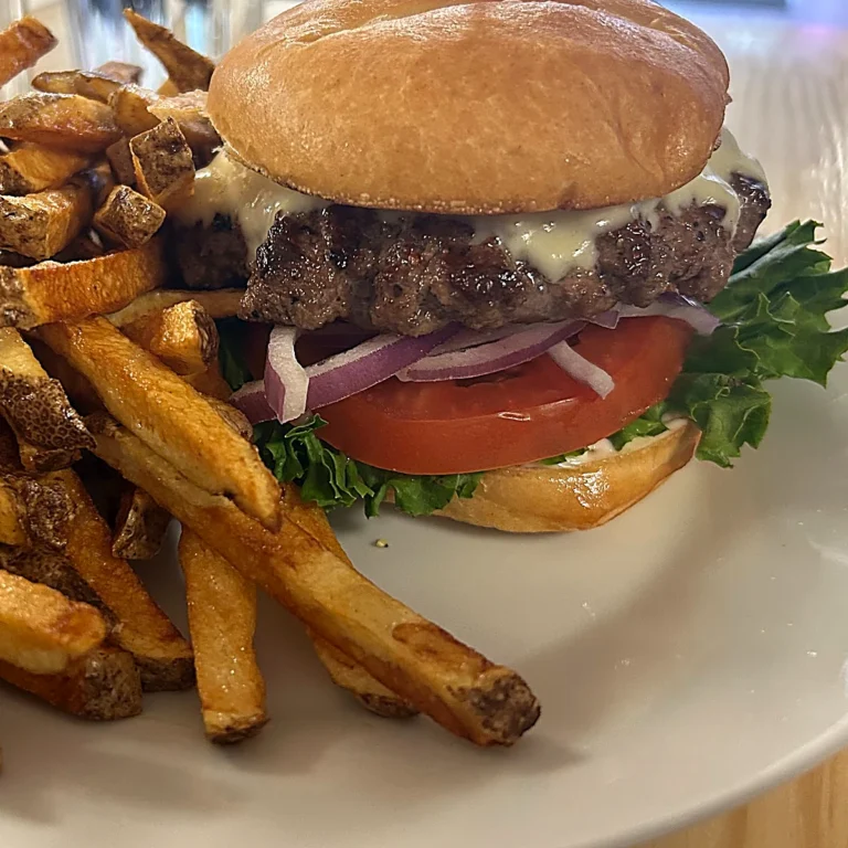 Smash burger with melted cheese, lettuce, tomato, and red onion on a toasted bun, served with crispy, fresh-cut fries on a white plate.