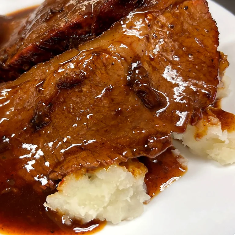 Sliced brisket with brown gravy served with mashed potatoes on a plate.
