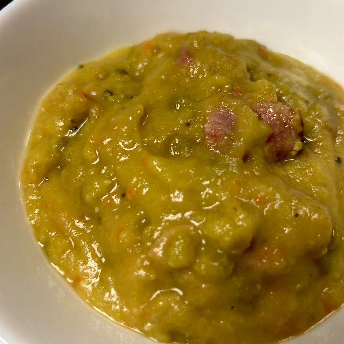 Close-up of thick split pea soup with visible chunks of ham in a white bowl.
