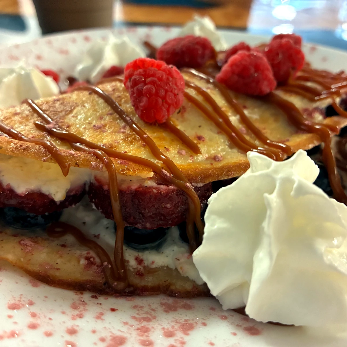 Sweet cheese crepe layered with fresh berries, topped with raspberries, a sauce drizzle, and whipped cream.