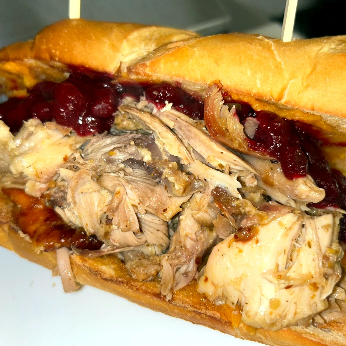 Thanksgiving carved turkey sub on a hoagie topped with homemade cranberry sauce, placed on a cutting board in the kitchen.