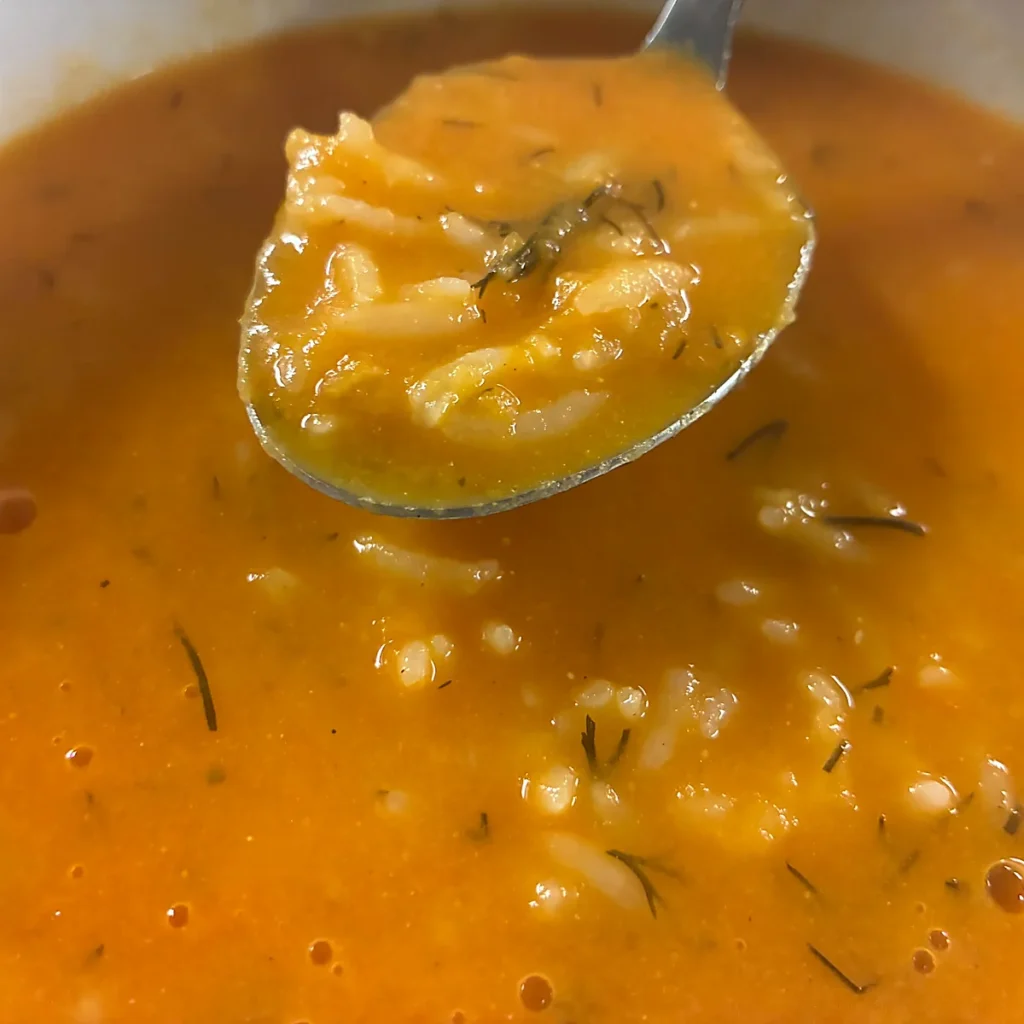 Creamy tomato soup with rice and herbs, shown in a spoonful above the bowl