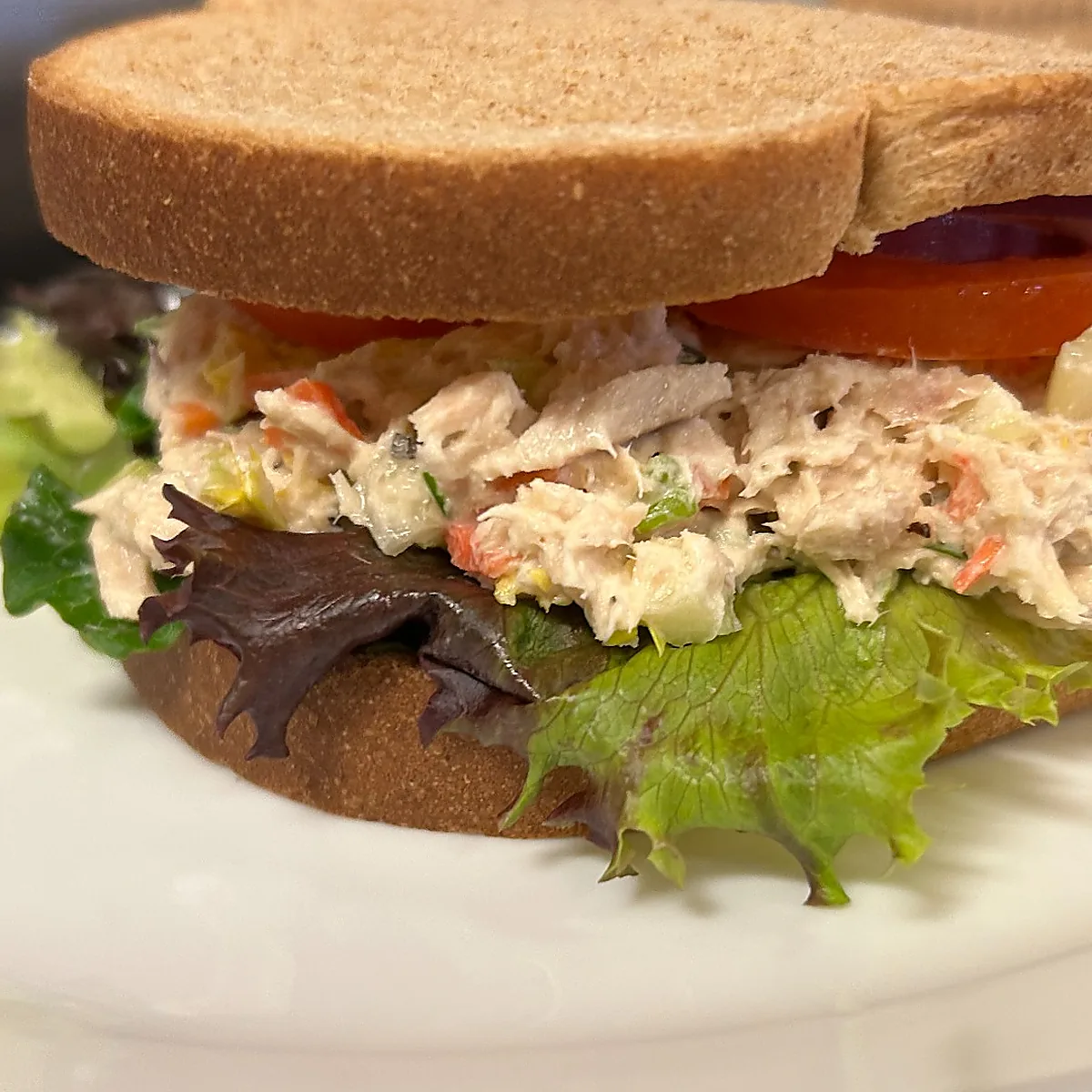 Close-up of a tuna salad sandwich on whole wheat with lettuce and tomato.