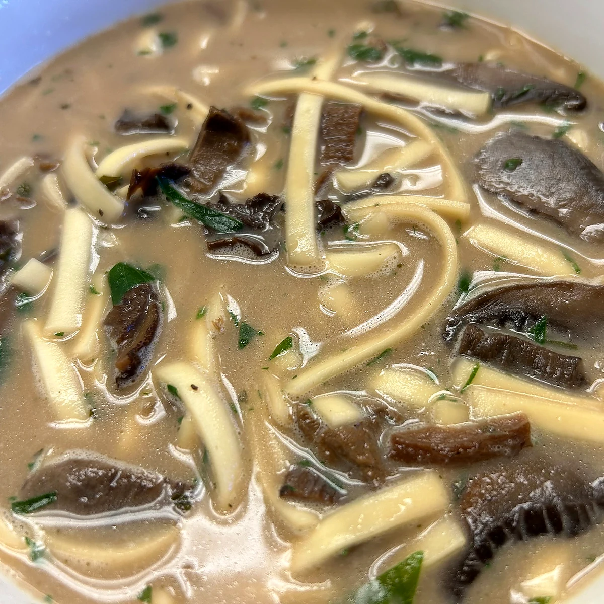 Creamy wild mushroom soup with noodles and herbs in a white bowl.