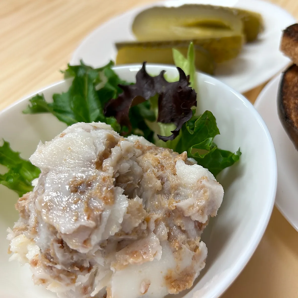 Bowl of seasoned lard spread with greens, served with toast and pickle slices in the background.