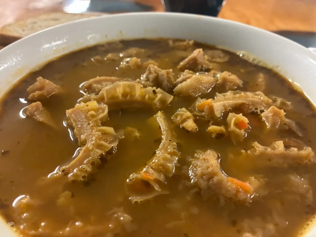 Beef tripe soup in a brown broth with tender tripe pieces in a white bowl.