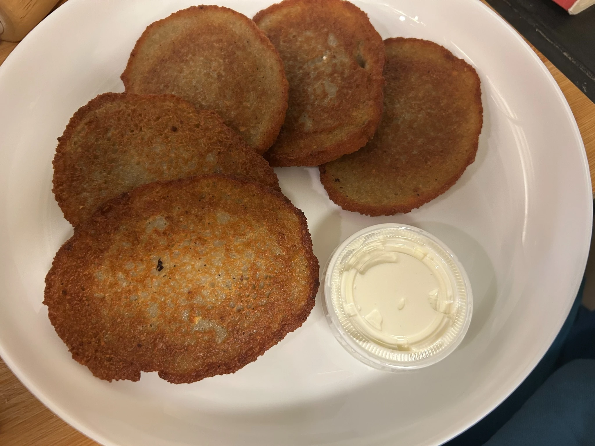 Five crisp potato blinis (bleenies) served on a white plate with a side of sour cream.