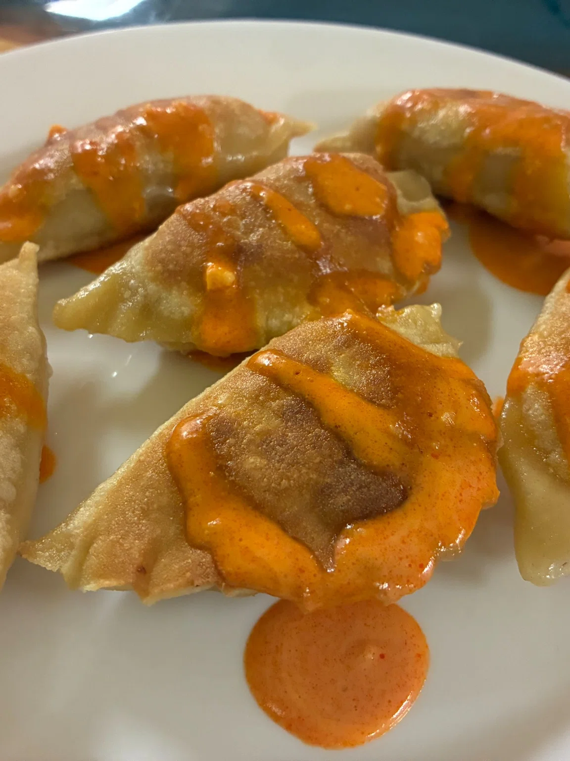 Pan-fried buffalo chicken pierogies served with a drizzle of homemade buffalo sauce on a white plate.