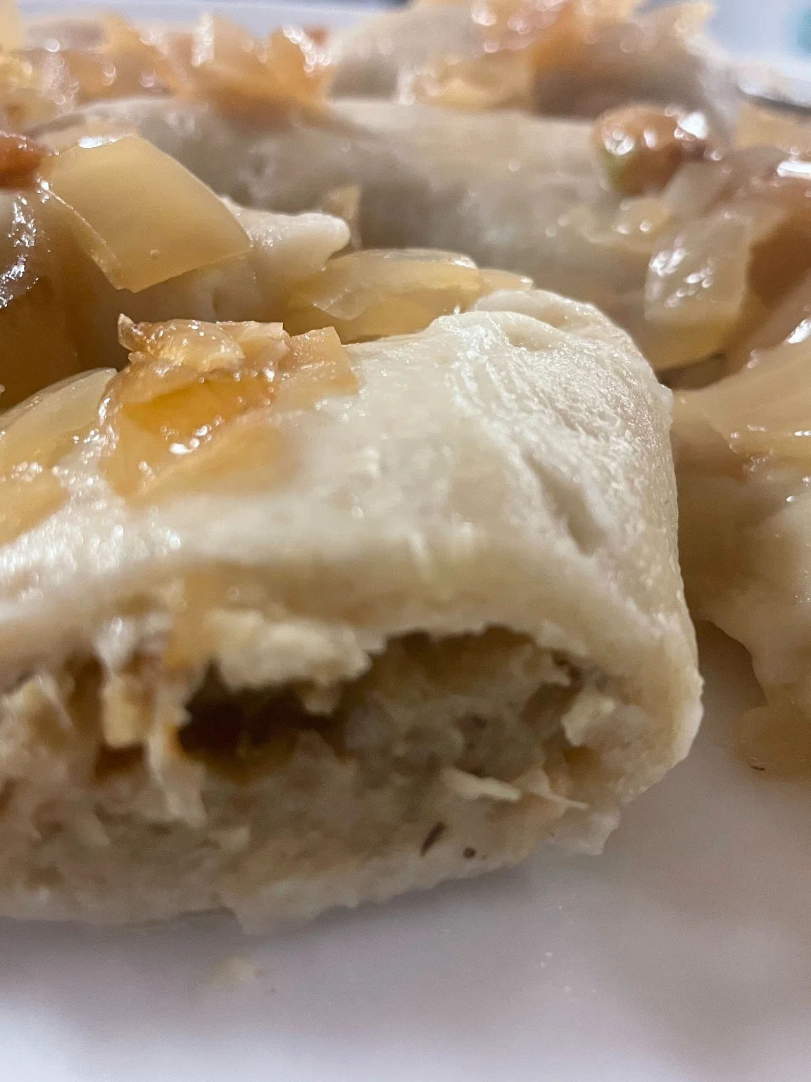 Cabbage and mushroom pierogies topped with sautéed onions on a white plate.