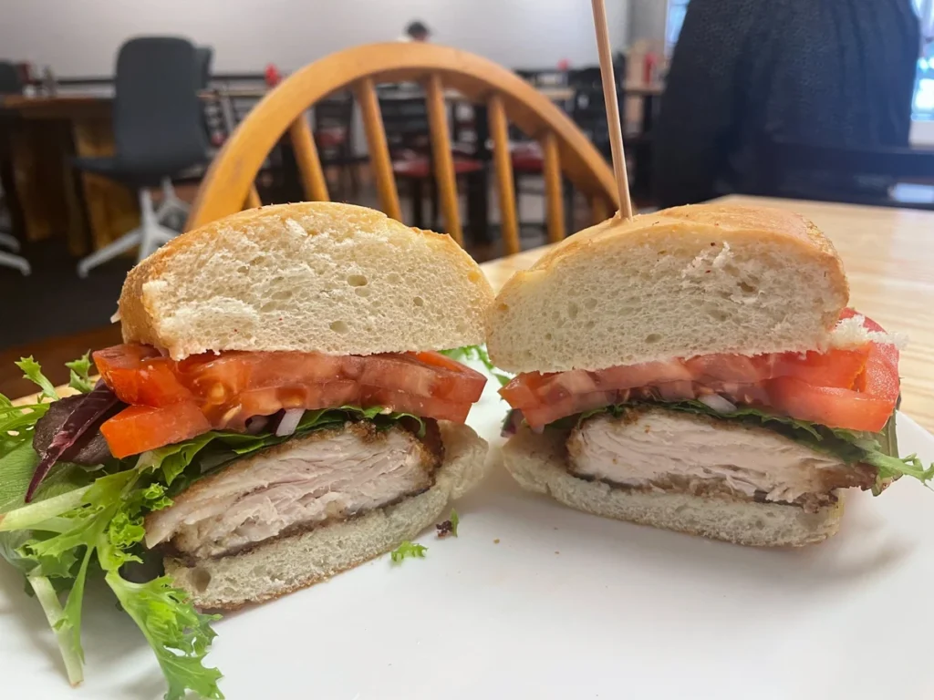 Chicken cutlet sub cut in half with breaded chicken, lettuce, tomato, and red onion on fresh hoagie bread at Kat's Café & Restaurant dining room.