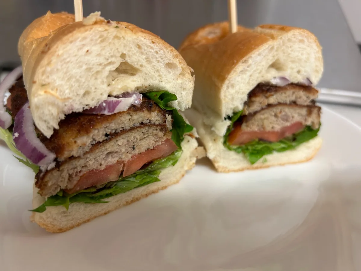 City chicken sub cut in half with breaded minced-meat patties, lettuce, tomato, red onion, and mayo on soft hoagie bread.