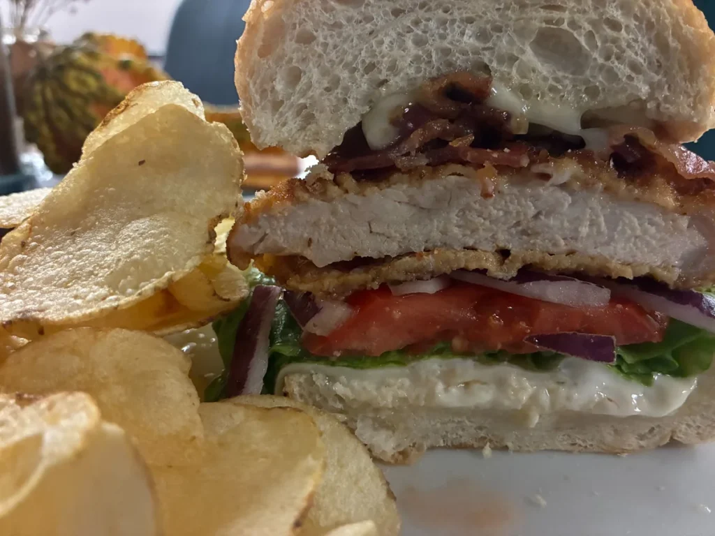 Pork schnitzel sub with breaded pork cutlet, lettuce, tomato, red onion, bacon, and melted cheese, served with chips.
