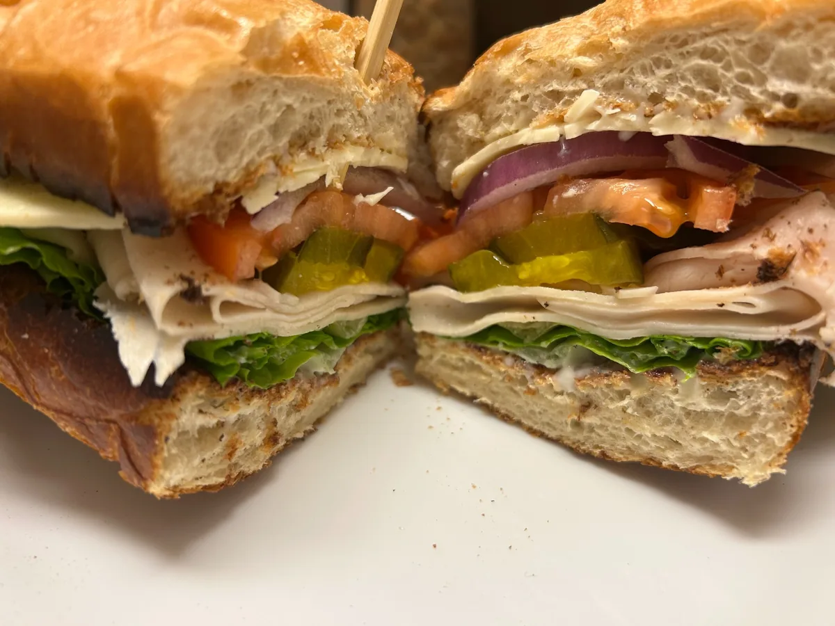 Roasted turkey sub cut in half with sliced turkey, lettuce, tomato, pickles, red onion, and swiss cheese on toasted hoagie bread.
