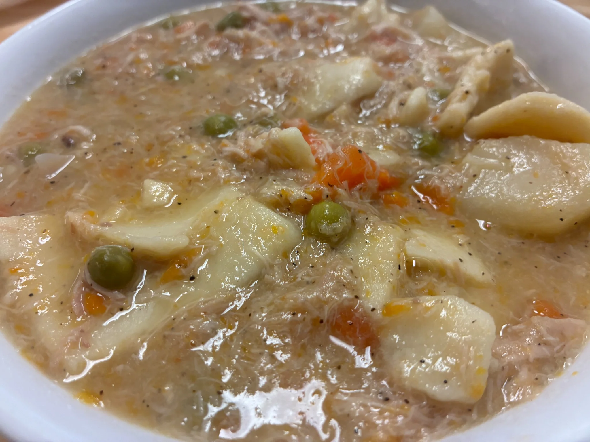 Creamy chicken pot pie soup with chicken, vegetables, and soft homemade dough squares in a white bowl.